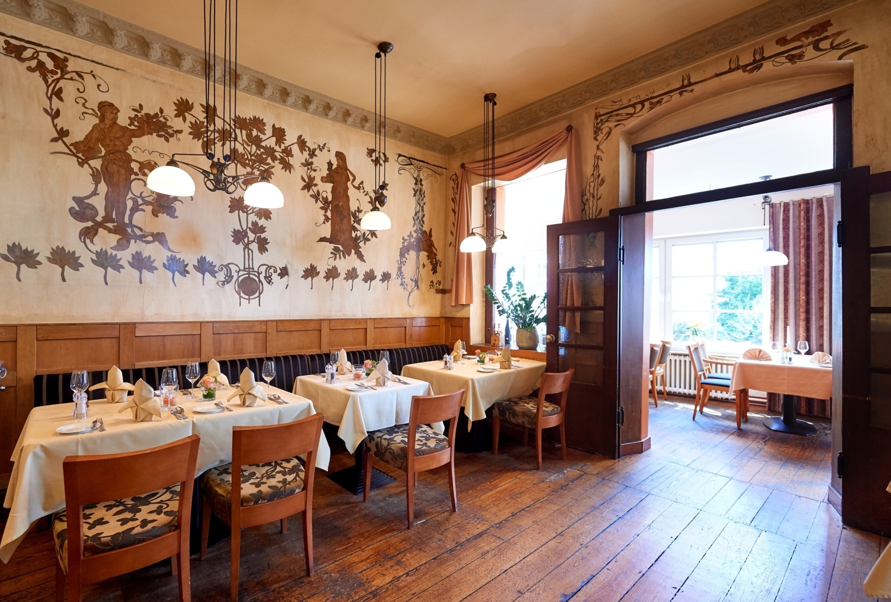 Eleganter Restaurant-Speisesaal mit Holzböden, dekorierten Wänden, gedeckten Tischen und warmer Umgebungsbeleuchtung.