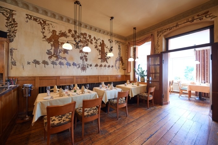 _SG56136 Eleganter Speisesaal des Restaurants mit Holzböden, kunstvoll verzierten Wänden, gedeckten Tischen und warmer Hängebeleuchtung.