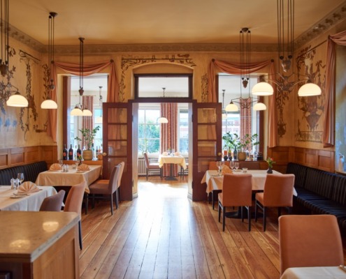 Eleganter Restaurant-Speisesaal mit Holzböden, gedeckten Tischen für Gäste, großen Fenstern und warmer Beleuchtung.