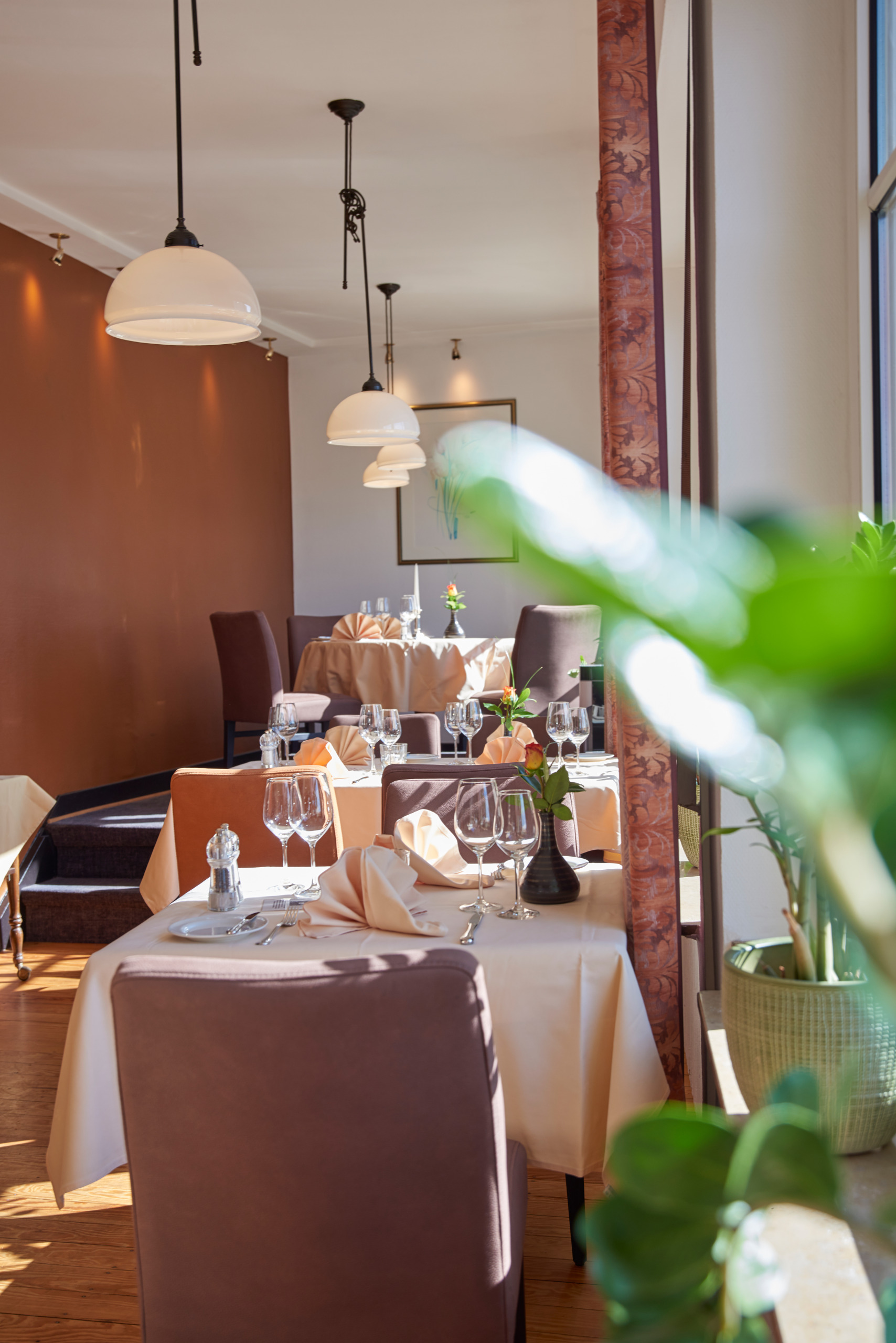 Helles, elegantes Restaurant mit gedeckten Tischen, braunen Stühlen, weißen Tischdecken und Sonnenlicht, das durch große Fenster strömt.