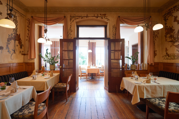 _SG56145 Elegantes Restaurant-Interieur mit Holzböden, dekorierten Wänden und ordentlich gedeckten Tischen, durch offene Türen blickt man in einen hellen Essbereich.