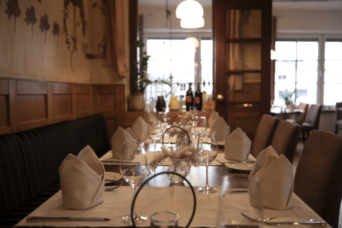 _DSC2149 (Groß) Eleganter Restauranttisch mit weißen Servietten, Weingläsern und Tellern in einem warm beleuchteten, gemütlichen Speisesaal.