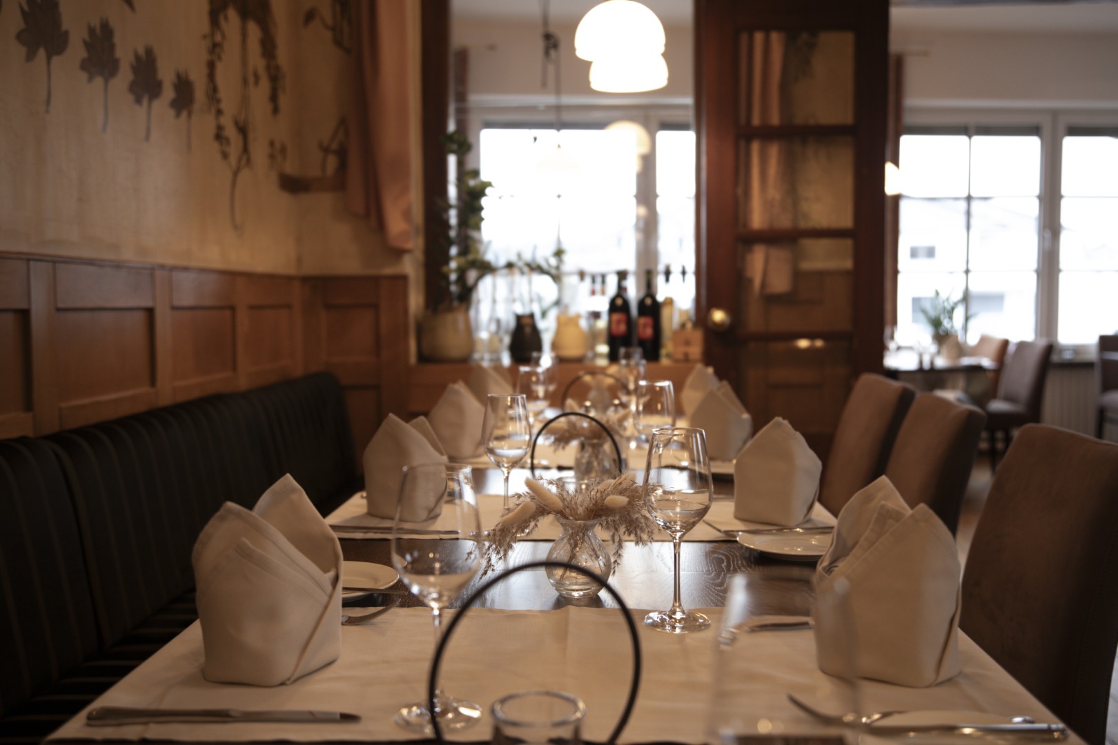 Eleganter Restauranttisch mit weißen Servietten, Weingläsern und Tellern in einem warm beleuchteten, gemütlichen Speisesaal.