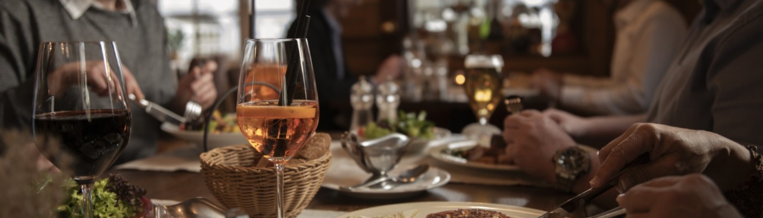 Menschen essen in einem Restaurant, genießen Getränke und Speisen und unterhalten sich an einem warm beleuchteten Tisch.