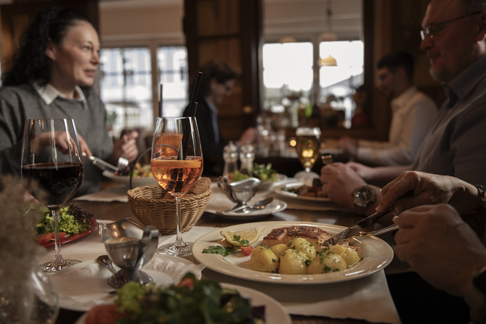 Menschen essen in einem Restaurant, genießen Getränke und Speisen und unterhalten sich an einem warm beleuchteten Tisch.