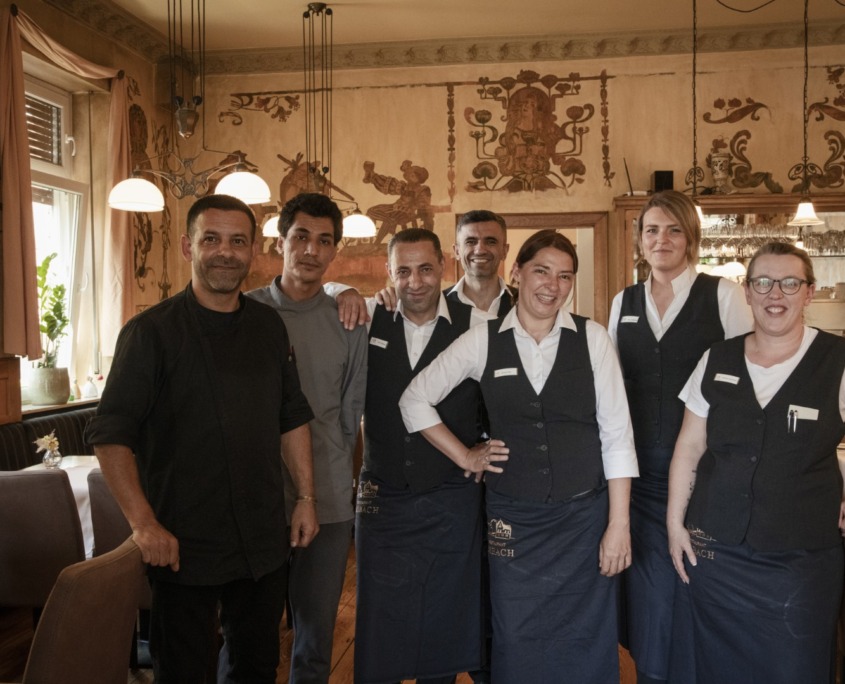 _DSC1551 (Groß) Eine Gruppe von sieben lächelnden Restaurantmitarbeitern posiert zusammen in einem warm beleuchteten Essbereich.